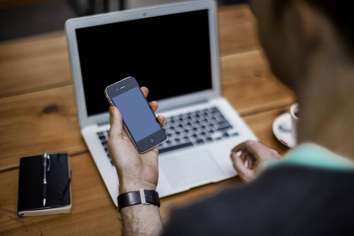 man holding cell phone at table with laptop booking junk removal